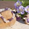 armband van ruwe amethist, rozenkwarts en bergkristal chips op een steen met paarse bloemen en gedroogde planten