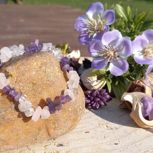 armband van ruwe amethist, rozenkwarts en bergkristal chips op een steen met paarse bloemen en gedroogde planten