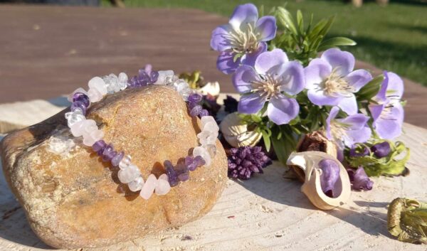 armband van ruwe amethist, rozenkwarts en bergkristal chips op een steen met paarse bloemen en gedroogde planten