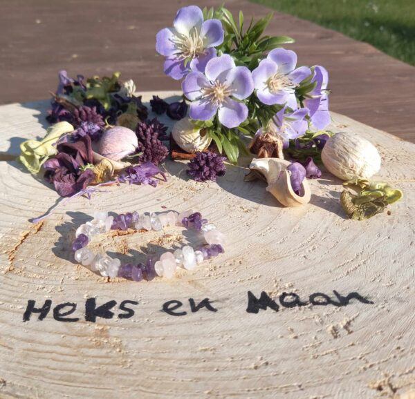 armband van ruwe amethist, rozenkwarts en bergkristal chips op een houten schijf met logo 'Heks en Maan', omringd door paarse bloemen en gedroogde planten