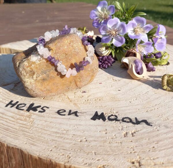 armband van ruwe amethist, rozenkwarts en bergkristal chips op een houten schijf met logo 'Heks en Maan', omringd door paarse bloemen en gedroogde planten