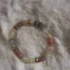armband van gefacetteerde, veelkleurige maansteen kralen in pastelkleuren, liggend op een pluizige witte ondergrond