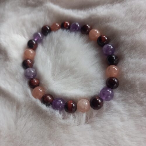 armband van ronde kralen in paarse (amethist), roodbruine (tijgeroog) en perzikkleurige (zonnesteen) edelstenen op een pluizige witte ondergrond