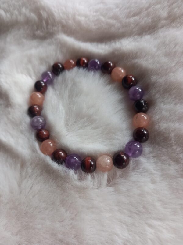 armband van ronde kralen in paarse (amethist), roodbruine (tijgeroog) en perzikkleurige (zonnesteen) edelstenen op een pluizige witte ondergrond