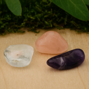 Gouden Driehoek edelstenen – amethist, rozenkwarts en bergkristal op licht houten ondergrond met groen mos en bladeren