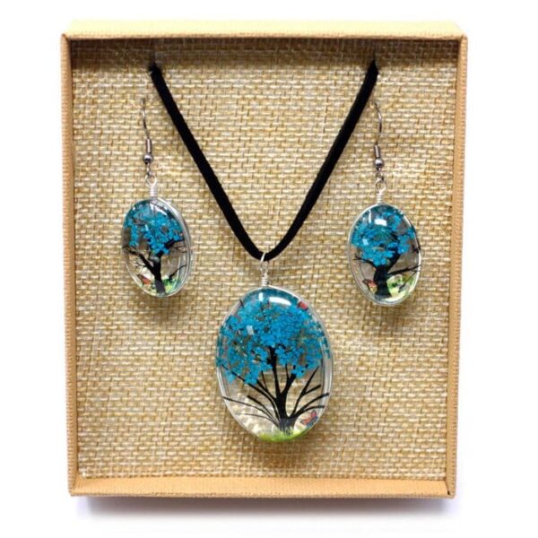Een Tree of Life sieradenset in tealblauw, met ketting en oorbellen van glas en gedroogde takjes, gepresenteerd in een beige doosje
