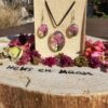 Een felroze Tree of Life sieradenset (ketting en oorbellen) met hars en gedroogde bloemen, gepresenteerd in een doosje op een boomstronk met bloemblaadjes en de tekst 'Heks en Maan'.