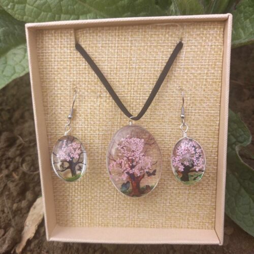 Tree of Life sieradenset in helder roze met een ketting en oorbellen, klaar om cadeau te geven, liggend in een doosje buiten in de natuur.