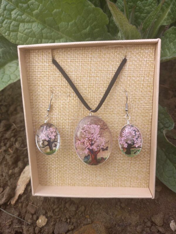 Tree of Life sieradenset in helder roze met een ketting en oorbellen, klaar om cadeau te geven, liggend in een doosje buiten in de natuur.