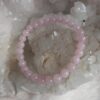 lichtroze rozenkwarts kralen armband liggend op een ruwe witte kwartskristal geode en pluizige ondergrond
