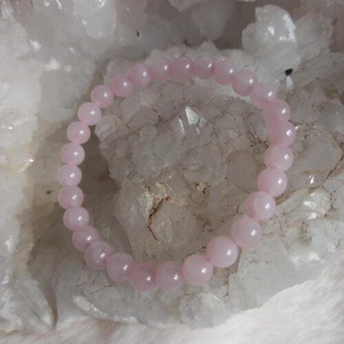 lichtroze rozenkwarts kralen armband liggend op een ruwe witte kwartskristal geode en pluizige ondergrond