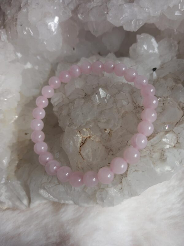 lichtroze rozenkwarts kralen armband liggend op een ruwe witte kwartskristal geode en pluizige ondergrond