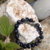 zwarte agaat kralen armband met witte strepen, liggend op ruwe witte en grijze stenen met groen blad