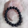 zwarte onyx kralen armband met matte finish, liggend op een ruwe rozenkwarts steen en pluizige witte ondergrond