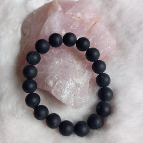 zwarte onyx kralen armband met matte finish, liggend op een ruwe rozenkwarts steen en pluizige witte ondergrond